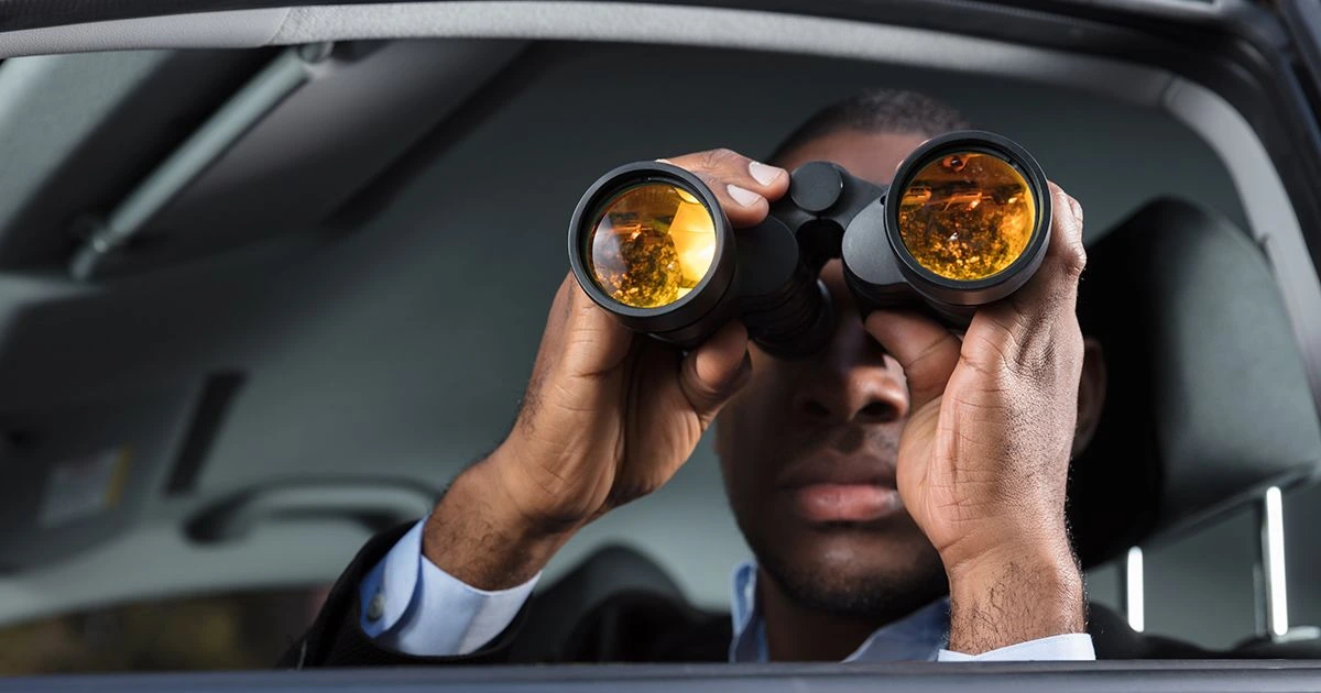 Man in car wearing suit holding binoculars up to his face
