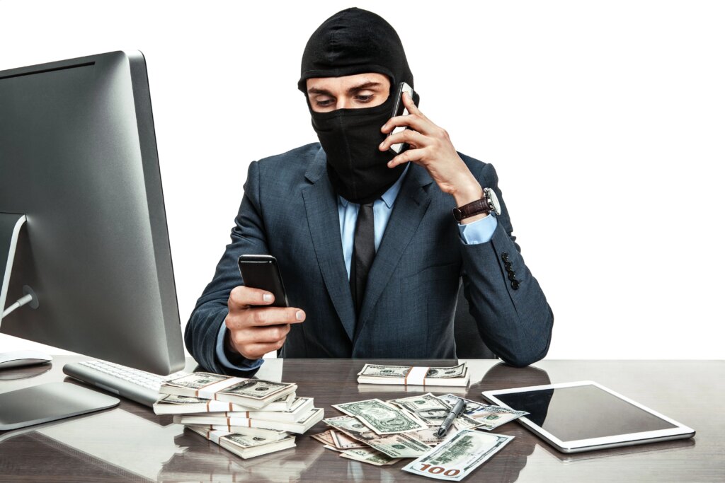 businessman wearing ski mask sitting at desk with piles of cash