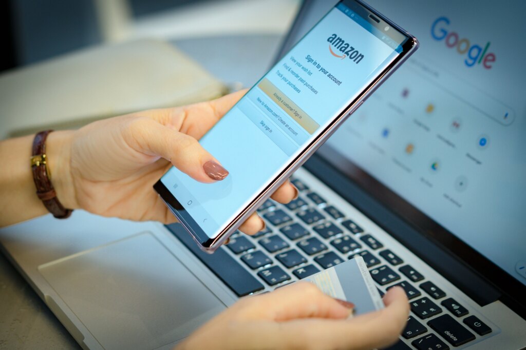 Hands holding credit card and phone (displaying Amazon) in front of laptop