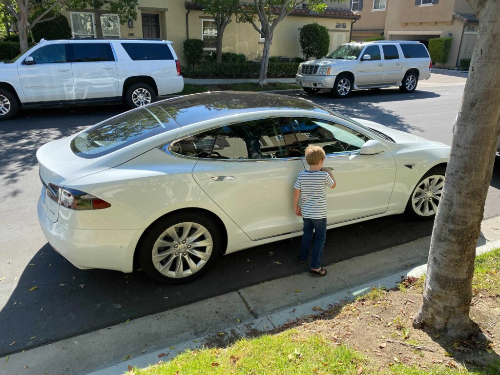 Nick's young son Jonas standing outside white Tesla on residential street